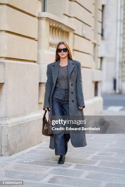 Diane Batoukina wears black Gucci sunglasses, a grey transparent top, a grey SourceUnknown coat, dark blue denim Massimo Dutti jeans / pants, a...