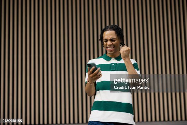 cheerful african american man reading good news over mobile phone. - punching the air stock pictures, royalty-free photos & images