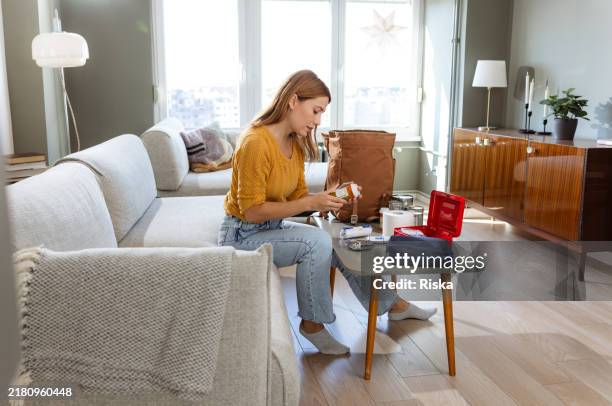 a woman assembling emergency supplies in living room - first aid kit stock pictures, royalty-free photos & images