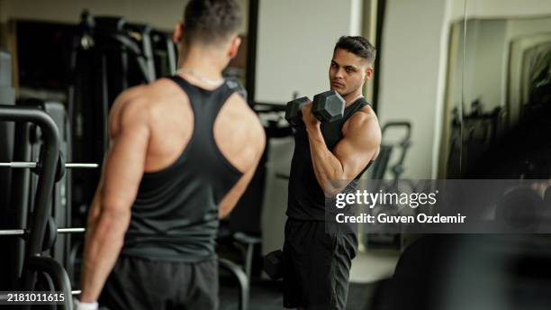 entusiasta del fitness perfeccionando su forma con curls de bíceps concentrados usando pesas libres, sesión intensa de entrenamiento de fuerza con atleta musculoso que realiza curls con mancuernas en un entorno de espejo de gimnasio, destacando la fuerza - flexionar los músculos fotografías e imágenes de stock