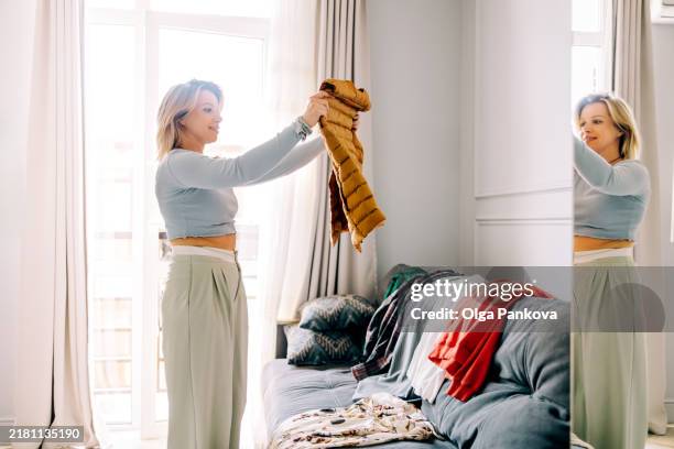 mid adult woman organizing wardrobe and trying on clothes at home - neat stock pictures, royalty-free photos & images
