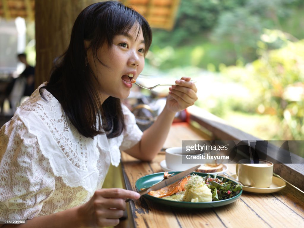 Asian woman eating pan fried salmon in cafe