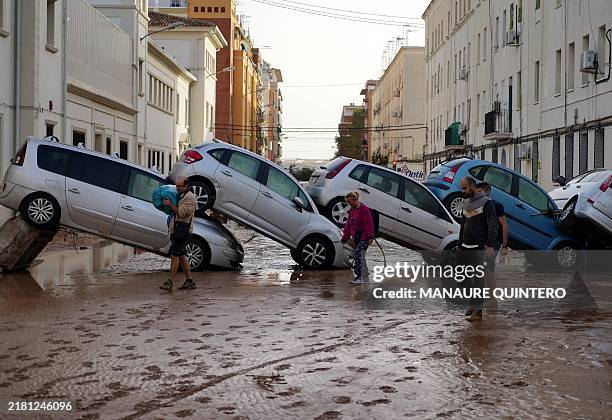 Residents walk past piled up cars following deadly floods in Valencia's De La Torre neighbourhood, south of Valencia, eastern Spain, on October 30,...