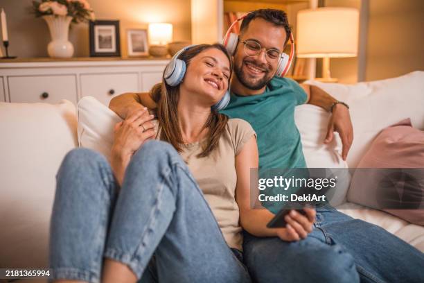 una pareja de enamorados escucha música desde un teléfono móvil con auriculares inalámbricos - pareja de mediana edad fotografías e imágenes de stock