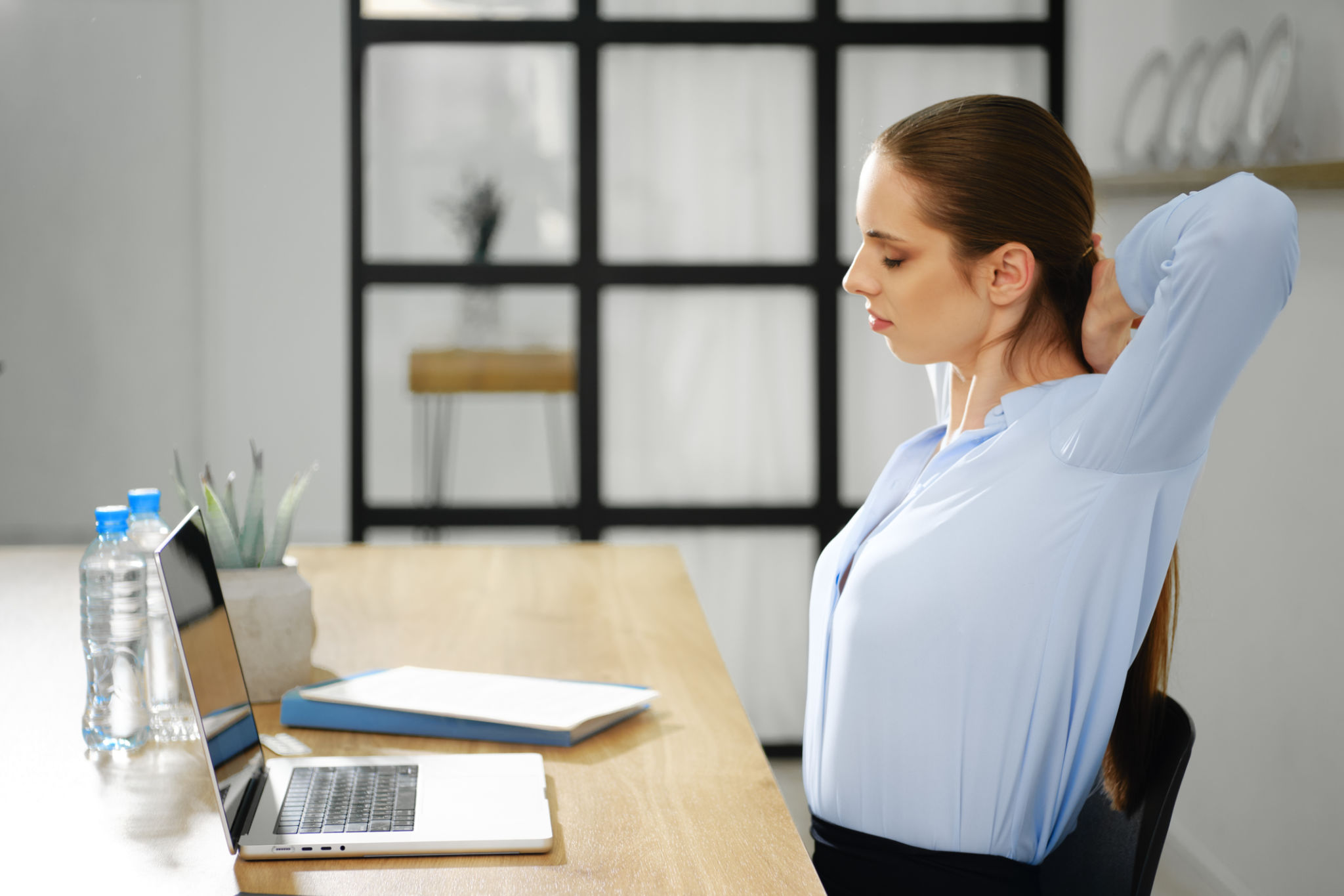 Woman stretching at a desk with a laptop, neck down Woman stretching at a desk with a laptop, neck down