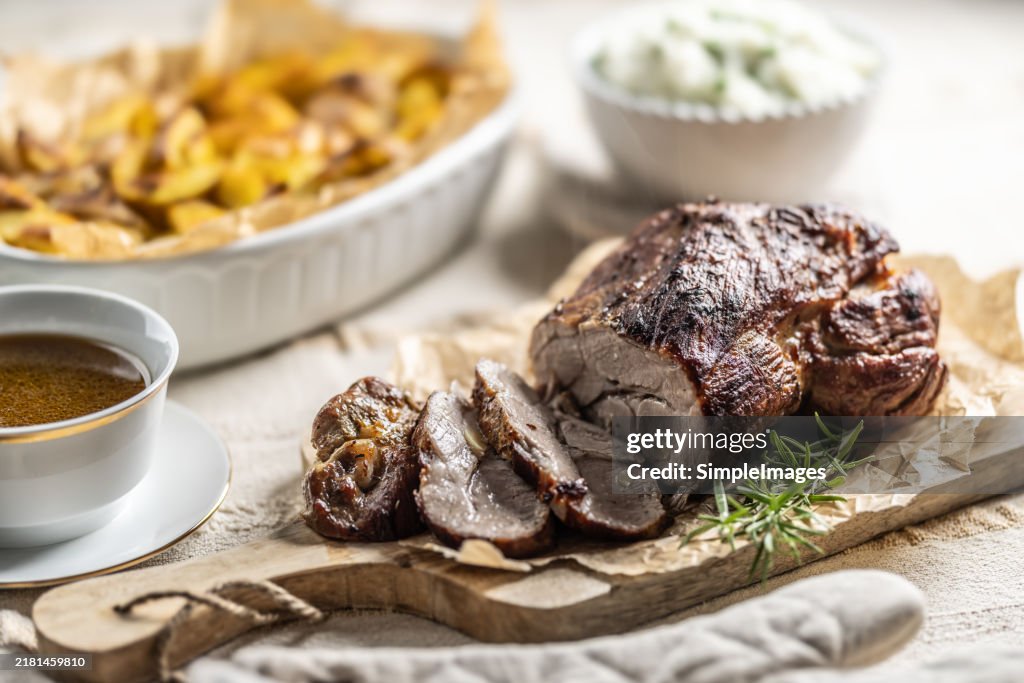 Roasted pork neck on a cutting board with side dishes, baked potatoes and pea jasmine rice and sauce