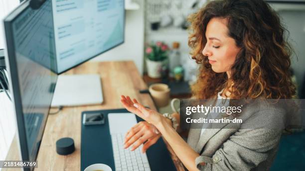 woman working at standing desk is using hand cream - carteira de pele imagens e fotografias de stock