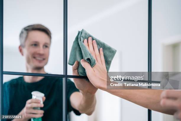 a young man wipes a mirror with a microfiber cloth - mikrofaser stock-fotos und bilder