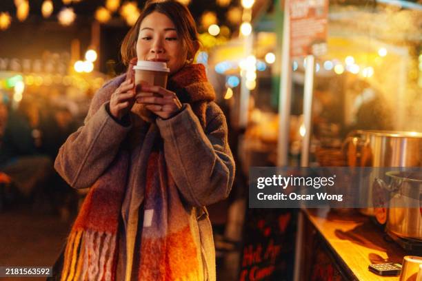 young asian woman buying mulled wine from market stall on christmas market - scarf stock pictures, royalty-free photos & images