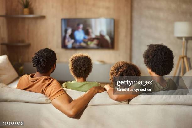 back view of a black family watching tv at home. - television stock pictures, royalty-free photos & images
