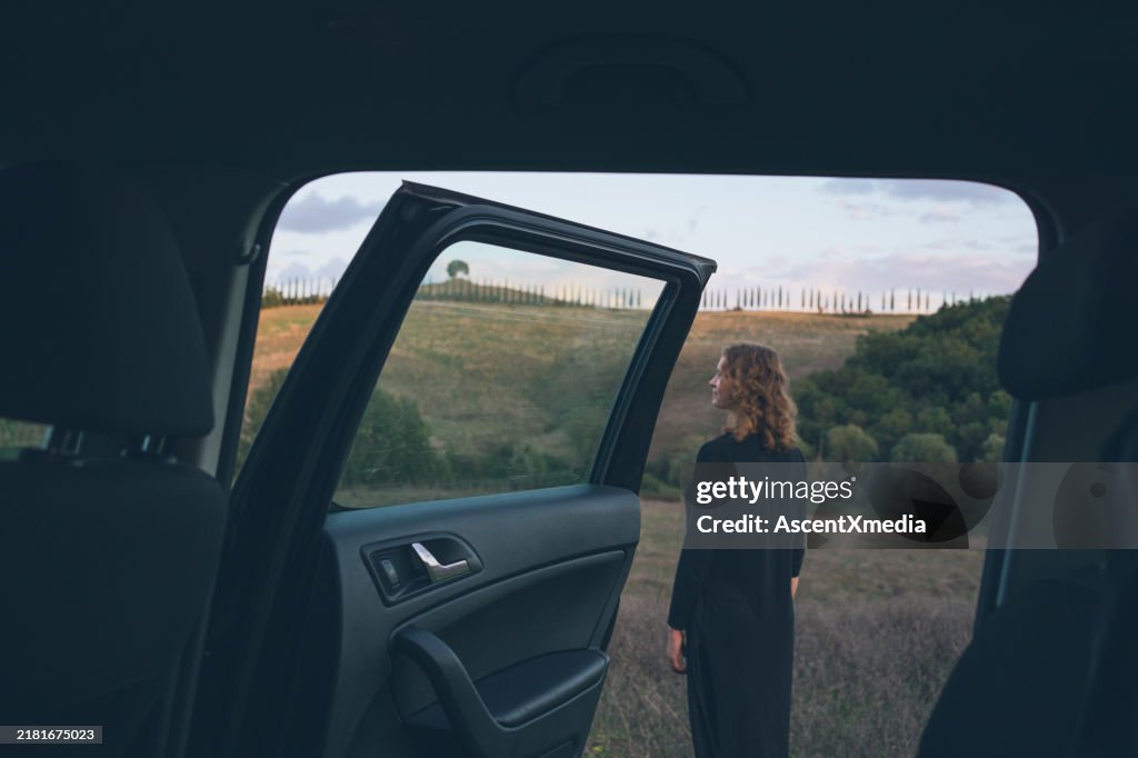 View through car door to rural landscape and young woman