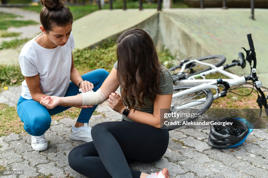 Worried Female Helping Her Fallen and Injured Friend by Wrapping Her Elbow in Bandage After Bike Accident