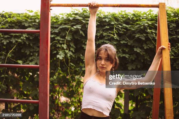 portrait of young woman hanging on horizontal bar at playground - gymnastics bar stock pictures, royalty-free photos & images