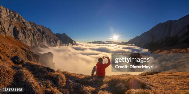 wanderer, der in den alpen sitzt, fotografiert mit handy von beeindruckender herbstlandschaft - freiklettern stock-fotos und bilder