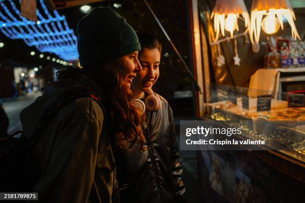 two women enjoy the christmas market in the city at night - night market stock pictures, royalty-free photos & images