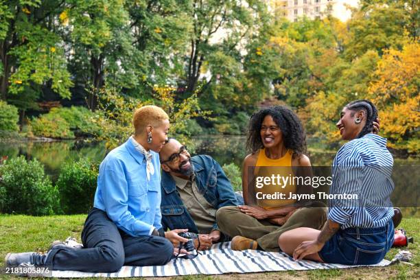 family relaxes and laughs sitting on blanket in public park - alte und junge lesbische frauen stock-fotos und bilder