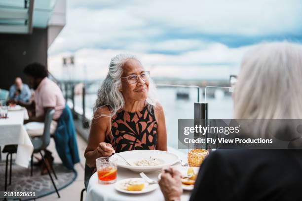 pacific islander senior woman having dinner with a friend - restaurant patio dining stock pictures, royalty-free photos & images