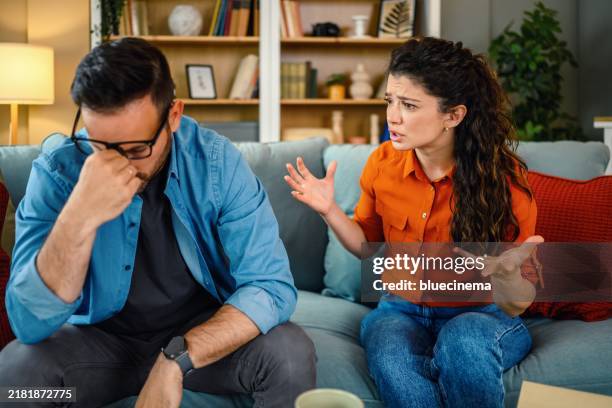 mid adult couple arguing on sofa at home. - kommunikationsproblem stock-fotos und bilder