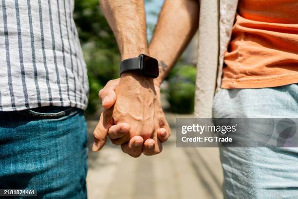 close-up of gay couple holding hands outdoors - gay man stock pictures, royalty-free photos & images