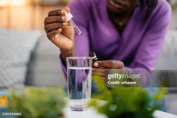 mujer joven poniendo gotas de medicina en un vaso de agua - cuentagotas fotografías e imágenes de stock