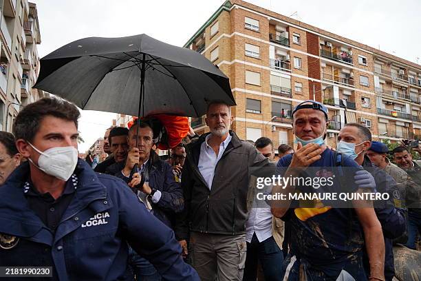 King Felipe VI of Spain is protected with an umbrella as angry residents heckle him and throw mud and objects during his visit to Paiporta, in the...