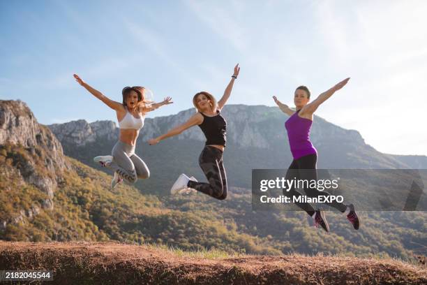 three women jumping outdoors in scenic mountain landscape - athleisure stock pictures, royalty-free photos & images