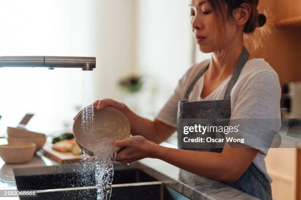 asian woman washing dishes in kitchen sink - washing dishes stock pictures, royalty-free photos & images