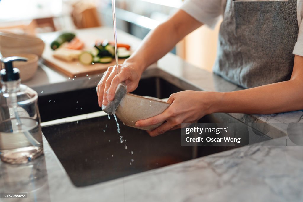 Closeup of female hand washing dishes in kitchen sink
