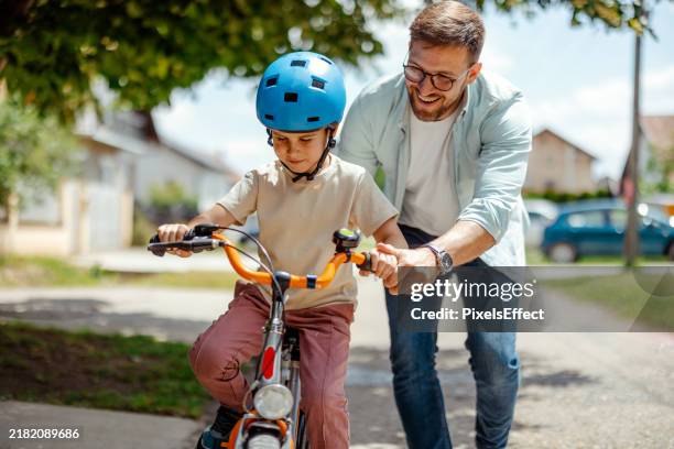 joyful father help his cute little to son ride a bicycle - cycling helmet stock pictures, royalty-free photos & images