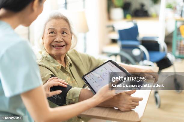 frau asiatische krankenschwester, die den blutdruck einer älteren patientin zu hause misst. häusliches pflegepersonal mit digitalem tablet - südostasien stock-fotos und bilder