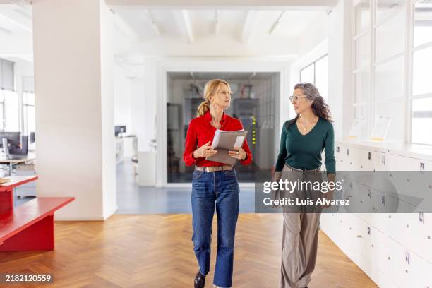 two mature businesswomen walking and discussing work in office - founder stock pictures, royalty-free photos & images