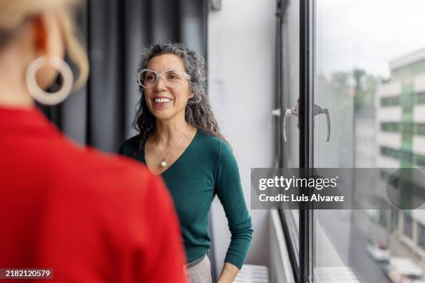 businesswomen standing in meeting room discussing work - face à face photos et images de collection