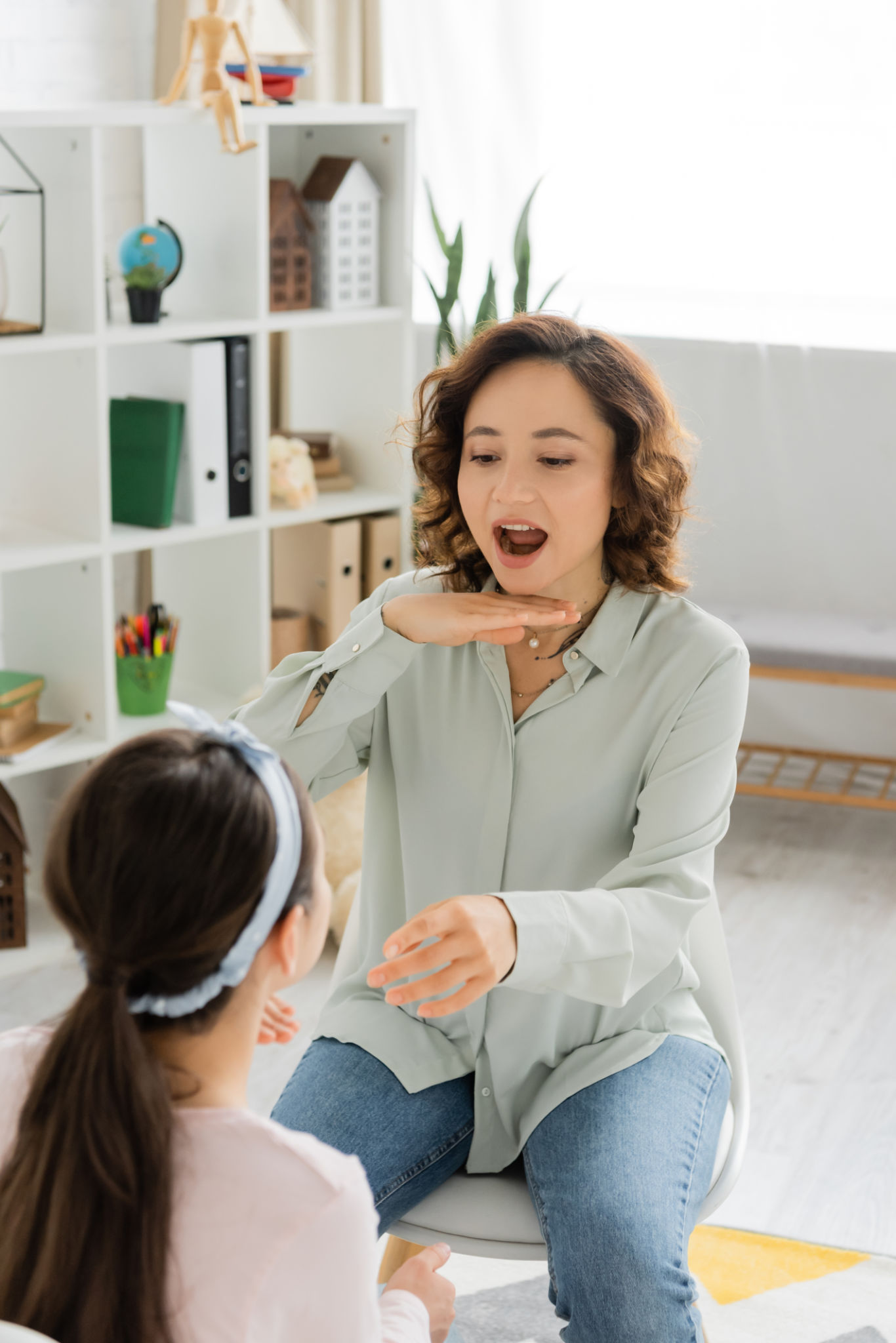 A caring speech therapist helps a child in a bright room to improve communication skills A caring speech therapist helps a child in a bright room to improve communication skills