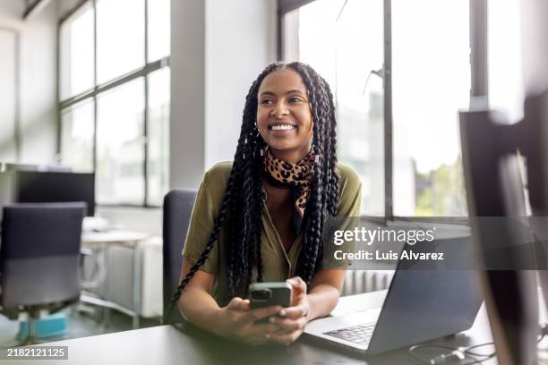 woman professional at her desk looking away and smiling at startup office - employee mobile phone stock pictures, royalty-free photos & images