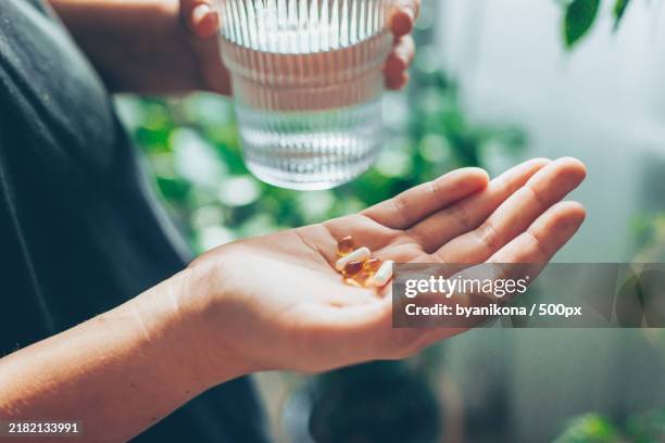 woman holding vitamins,pills or capsules on hand and a glass of water wellness,wellbeing concept - nahrungsergänzungsmittel stock-fotos und bilder