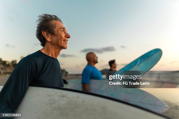 senior surfer man contemplating on the beach - baby boomer stock pictures, royalty-free photos & images