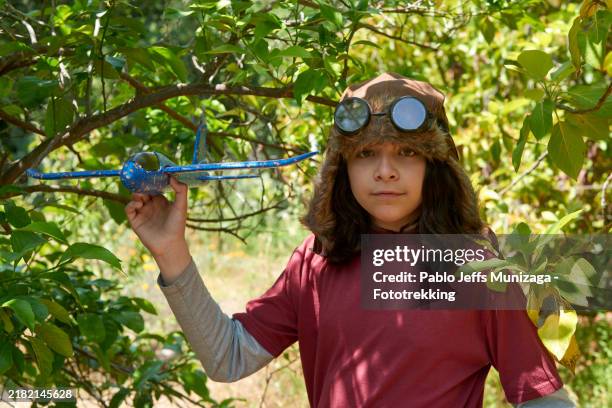 teenager with aviator hat holding toy plane in forest - aviation hat stock pictures, royalty-free photos & images