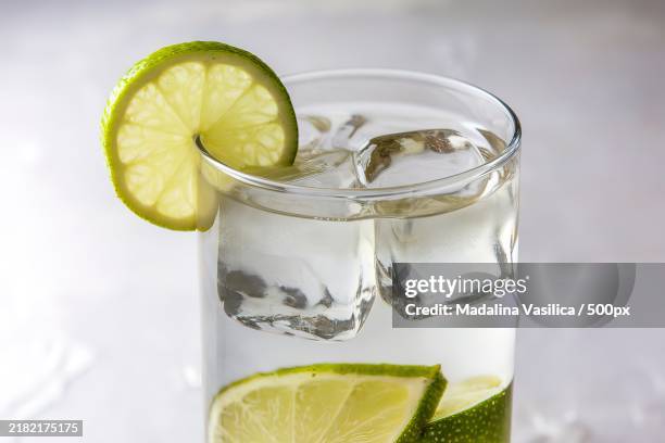 a photo of a gin and tonic drink with a lime wedge and ice cubes - tonic water stock pictures, royalty-free photos & images