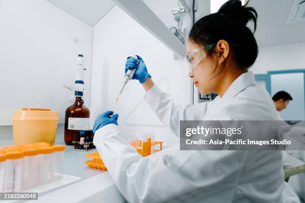 side-shot of asian female scientist filling chemical through pipette while working in modern laboratory. - person of colour stock pictures, royalty-free photos & images