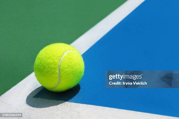sport concept with tennis ball on hard blue and green colour tennis court line marking background with shadow. - tennisball stock-fotos und bilder