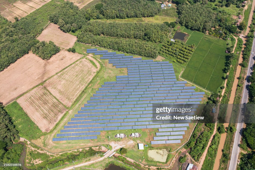 An aerial view reveals a vast expanse of solar panels arranged in orderly rows, stretching across the field and emphasizing a sense of immense scale and openness.