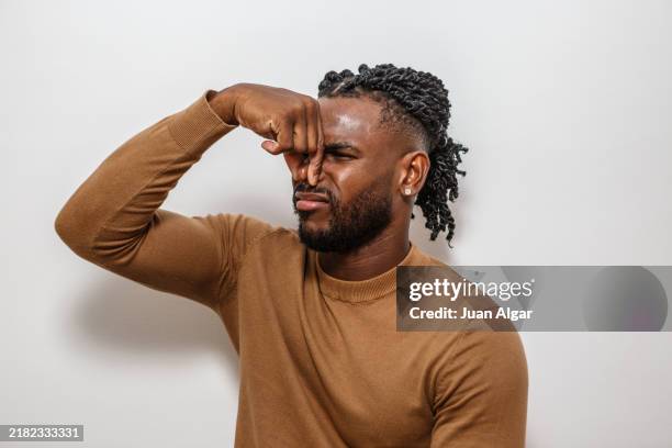 man pinching his nose in response to an unpleasant smell indoors during a casual moment - smelling stock pictures, royalty-free photos & images