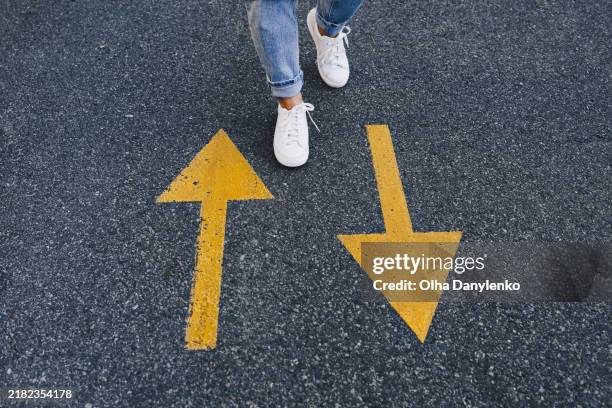 person walking between opposite yellow arrows on asphalt road - choisir photos et images de collection
