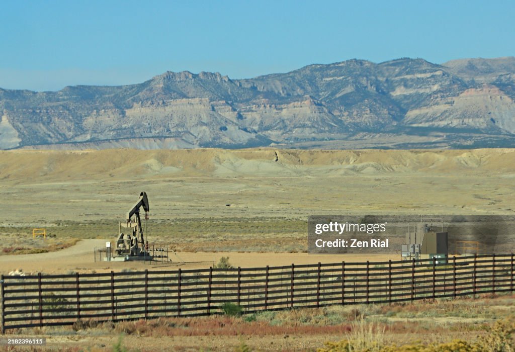 Landscape showing an oil pump, mountains in background, fence in foreground