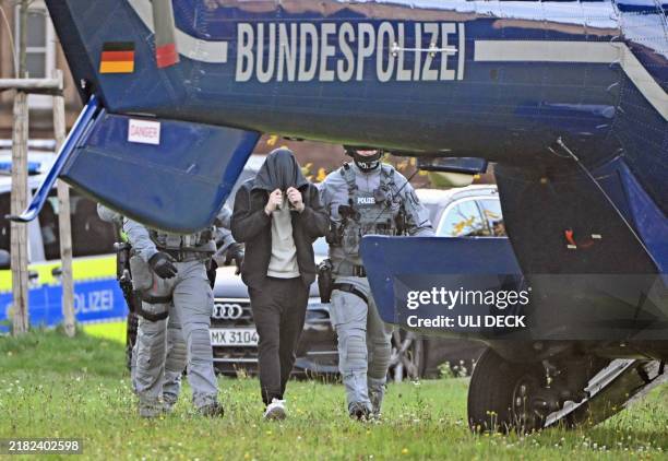 Policemen escort a man, one of eight suspected members of a militant group, after he was heard at the Federal Court of Justice towards a helicopter...