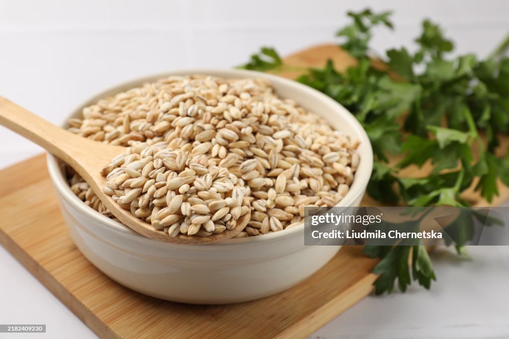 Dry pearl barley in bowl and wooden spoon on table, closeup