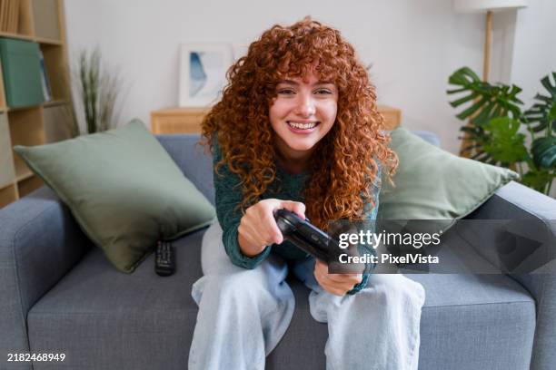 young woman playing videogames on sofa at home - videospel stockfoto's en -beelden