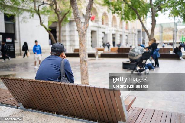 young man using phone while sitting on the park bench - park bench stock pictures, royalty-free photos & images