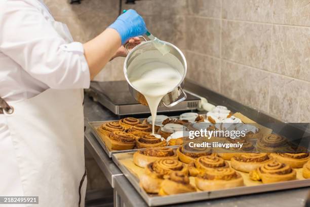 chef de pastelaria derramando molho em pãezinhos de canela - coberto de camada lustrosa - fotografias e filmes do acervo