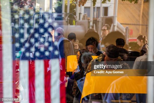 People cast their ballots at Joslyn Park vote center while voters standing in line are visible in the window reflection on November 5, 2024 in Santa...